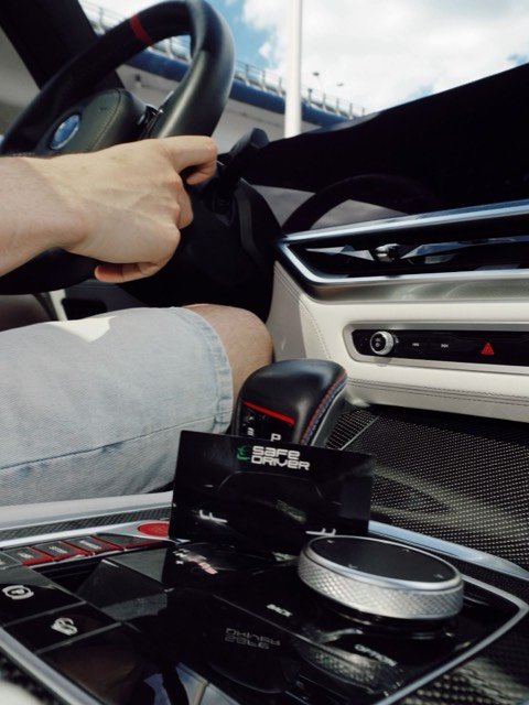 Водитель за рулём BMW, на консоли визитка Safe Driver